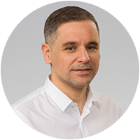 A man in a white shirt with short hair smiles slightly against a plain background.