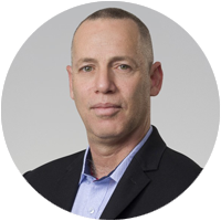 Avihay Ayash, a man with short hair, wearing a black blazer and light blue collared shirt, poses in front of a plain light gray background.